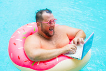 Laughing Fat Funny Man In Pink Inflatable Circle In Pink Glasses Works On A Laptop In A Swimming Pool