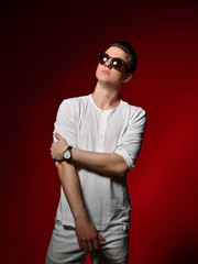 Elegant young handsome man in elegant casual dress and sunglasses in the studio on a red background.