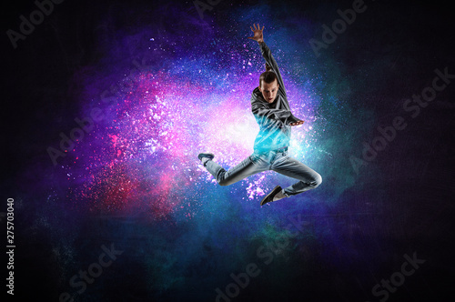 Modern female dancer jumping in hoodie with colourful splashes background. Mi...