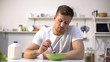 Unhappy lonely man looking with disgust at food in bowl, lack of appetite