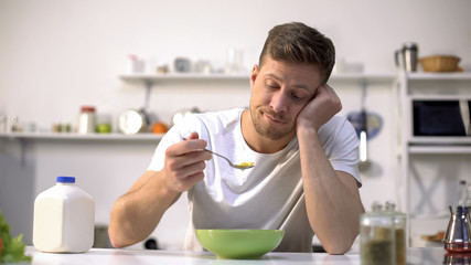 Upset single man eating tasteless cereals for breakfast, lack of appetite