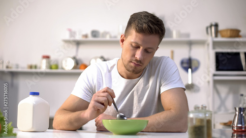 Cuadros en Lienzo Unhappy lonely man looking with disgust at food in bowl, lack of appetite