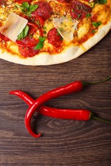 Two red hot chili peppers, pizza and mushroom on a brown wooden table. Mexican, Italian food. Top view. Capsaicin.