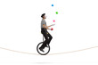 Mime riding a unicycle on a rope and juggling with balls