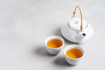 Wall Mural - Tea concept with white tea set of cups and teapot surrounded with fresh tea leaves on concrete background with copy space.