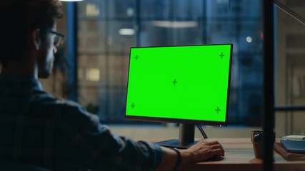 Wall Mural - over the shoulder: creative young man sitting at his desk using desktop computer with mock-up green 
