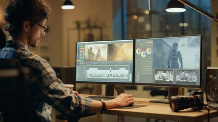 Wall Mural - late evening creative office: professional videographer works on desktop computer, doing footage mon