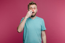 Studio Picture From A Young Man Uses Nose Spray. Sick Guy Isolated Has Runny Nose. Man Makes A Cure For The Common Cold