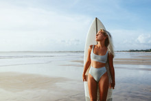 Surf Girl With Long Hair Go To Surfing. Young Surfer Woman Holding Blank White Short Surfboard On A Beach At Sunset Or Sunrise.