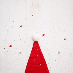 Wall Mural - Closeup of a Santa Claus Hat lying on a white wooden table with scattered shiny stars. New year, Christmas, holiday concept