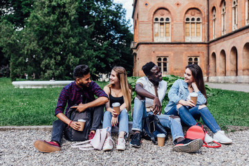 Wall Mural - After lessons. Students are sitting on the grass near university. Drinking coffee. Taking break from studying.