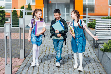 Wall Mural - Three elementary  and folders ,school students with backpacks on the street. Spend time tpgether.