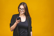 © denis_vermenko - Portrait of smiling business woman in eyeglasses holding smartphone and looking back over yellow background. Using phone.