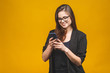 © denis_vermenko - Portrait of smiling business woman in eyeglasses holding smartphone and looking back over yellow background. Using phone.