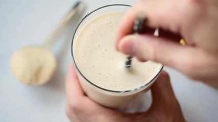 Wall Mural - Hand mixing protein smoothie with drinking straw. Closeup view