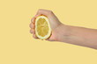 Woman's hand squeezing a lemon isolated on yellow background