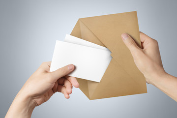 Hands pulling two blank sheets of paper (tickets, flyers, invitations, coupons, banknotes, etc.) out a brown envelope on gray background