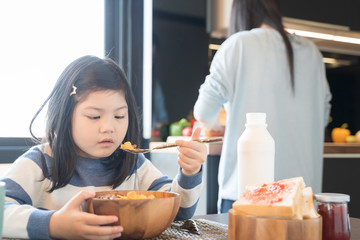 Wall Mural - mom and daughter eating Cereals with milk having breakfast in kitchen.