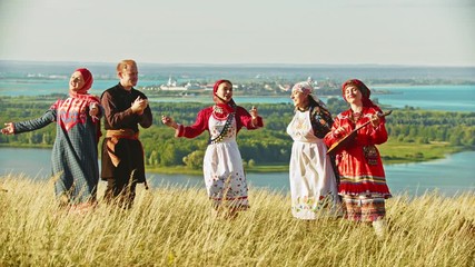 Wall Mural - Young ensemble in traditional russian clothes dancing on the field by the music