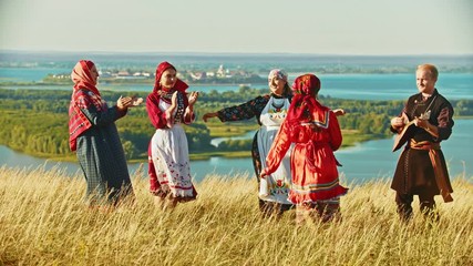 Wall Mural - Young ensemble in traditional russian clothes dancing on the field