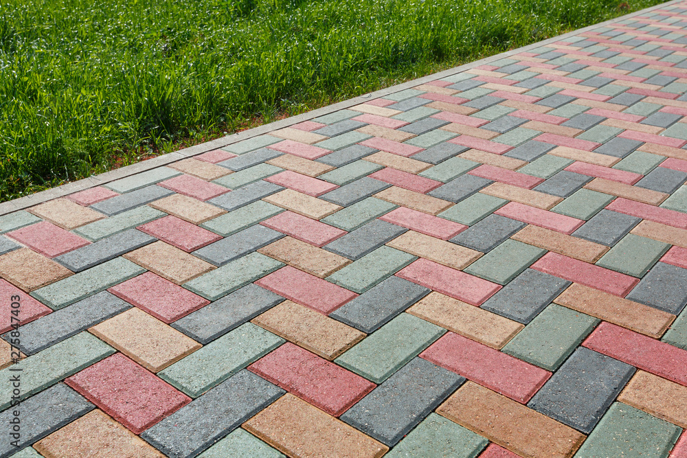 Colorful cobblestone road pavement and lawn divided by a concrete curb. - obrazy, fototapety, plakaty 