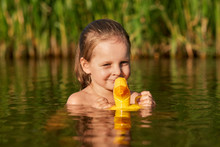 Good Looking Positive Child Swimming In Local Lake Alone, Holding Her Rubber Duck For Water, Enjoying Summer Holidays, Swimming Near Reed, Being In High Spirits. Children And Water Games Concept.