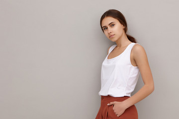 Isolated shot of attractive cute young Caucasian female model dressed in stylish clothes standing against blank studio wall background with copyspace for your text or advertising information