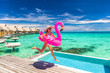 © Maridav - Vacation fun woman in bikini with funny inflatable pink flamingo pool float running of joy jumping by infinity swimming pool. Girl enjoying travel holidays at resort luxury overwater bungalow travel.