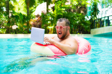 Screaming Funny Fat Male In Pink Glasses On An Inflatable Circle In The Pool Works On A Laptop Portraying A Girl.