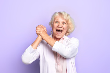 Old blonde woman keeping hands, palms together , rejoicing at good news, winning of favourite team, light blue background. happiness. close up photo.emotion and feeling.fan. emotion and feeling