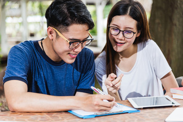 Man students and girlfriend are during reading information from tablet and book outdoor