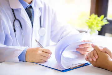 Doctor man consulting patient while filling up an application form at the desk in hospital. Medicine and health care concept