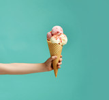 Fototapeta Sport - Baby kid hand holding big ice-cream in waffles cone on blue