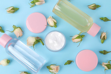 Cosmetics for face and body in pink bottles with fresh roses on a gentle blue background. creams and lotion. spa. top view