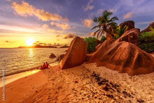Fotomural An identified romantic couple on shoreline near shaped granite stones of Anse Source d'Argent with sunset sky