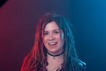 Youth, hairstyle and modern concept - young woman with dreadlocks smiling over the red and blue light background