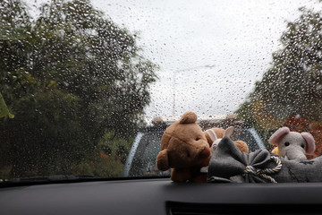 Doll in front of the car with atmosphere when it rains and background raindrops on car glass.