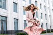 women's jacket and long skirt pleated coral, peach color. The girl is very emotional walking along the street. Long wavy hair flying in motion