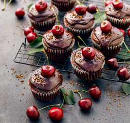 Cherry-Chocolate-coffee muffins with melted dark chocolate topping with the addition of fresh cherries on a cooling tray on a dark background, close-up. Delicious dessert