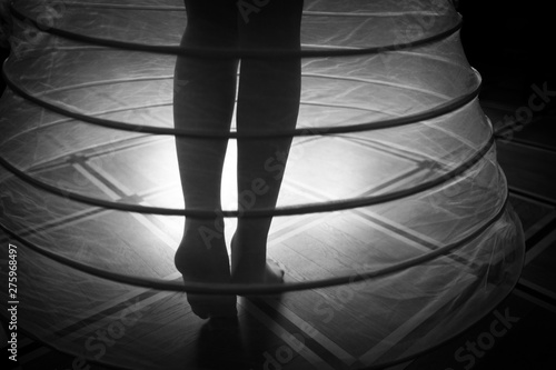 Fotografía Bare feet of a woman in a crinoline under the beam of light, black and white sho