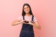 © Asier - Young pretty arab woman wearing a jeans dungaree smiling and showing a heart shape with hands.