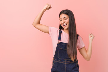 Wall Mural - Young pretty arab woman wearing a jeans dungaree raising fist after a victory, winner concept.