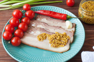 Baked pork belly or bacon sliced into thin slices on a plate with tomatoes, poured with mustard.