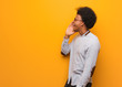 Young african american man over an orange wall whispering gossip undertone