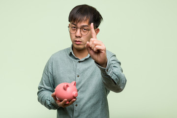 Young asian man holding a piggy bank showing number one