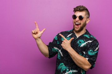 Young man wearing a vacation look pointing with forefingers to a copy space, expressing excitement and desire.