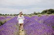 Beautiful young woman in a white dress and straw hat walks in the lavender field. Rear view.