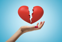 Side Closeup Of Woman's Hand Facing Up And Levitating Red Broken Heart On Light Blue Gradient Background.
