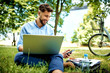 © baranq - Happy young businessman using laptop and phone while sitting in the park during lunch break