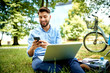 © baranq - Young entrepreneur sitting in park with laptop and bicycle using smartphone